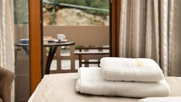 Una cama bien hecha con toallas blancas dobladas y vistas a una terraza exterior con una mesa y sillas.