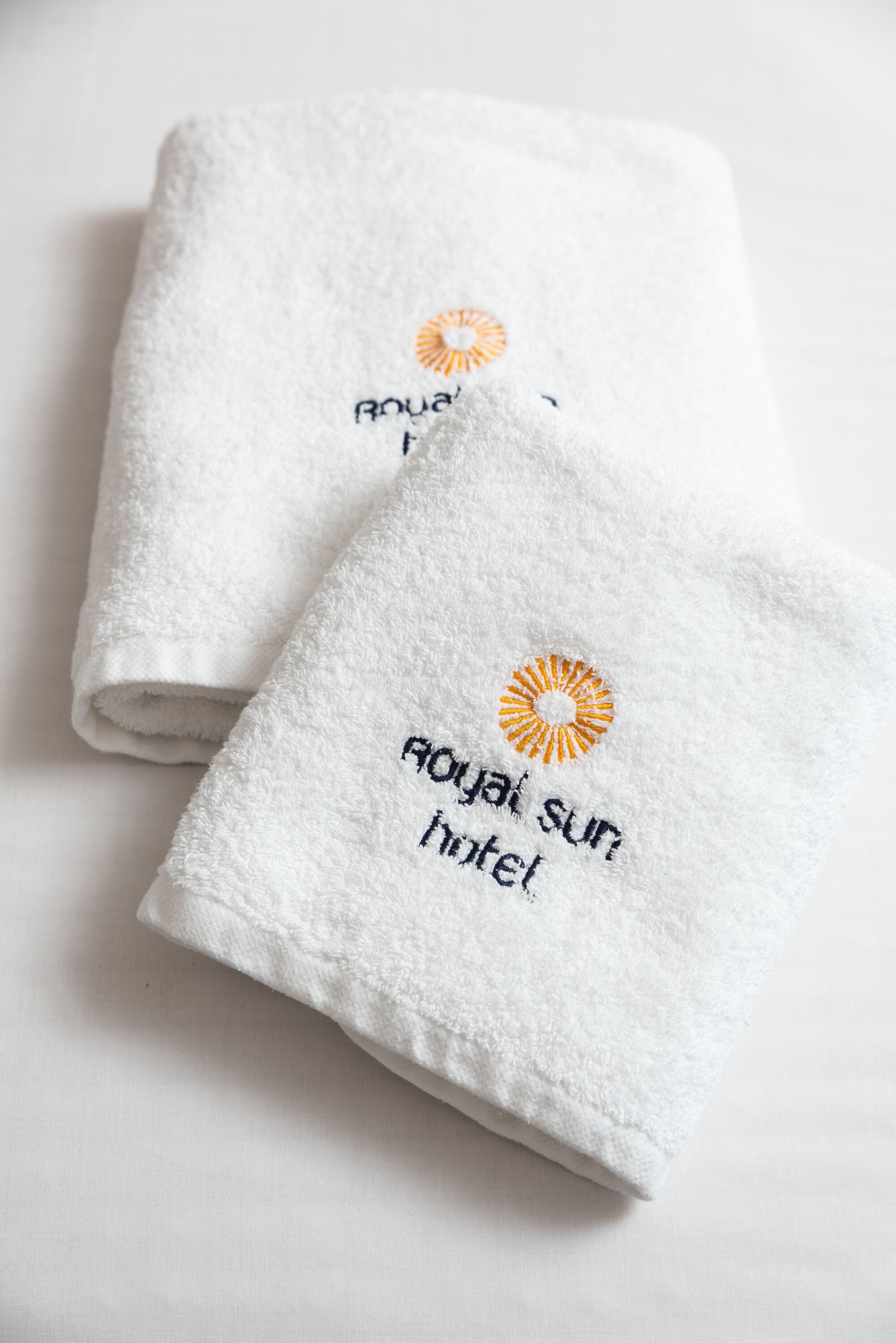 Two folded white towels with embroidered text and a sun design.