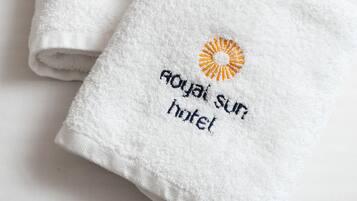Deux serviettes blanches pliées, ornées d’un motif brodé représentant un soleil et d’un texte.