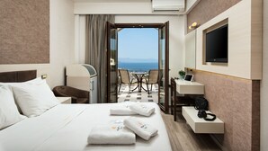 A hotel room with a bed, a desk, a chair, a TV, and a view of the sea. - Royal Sun Hotel (Chania)