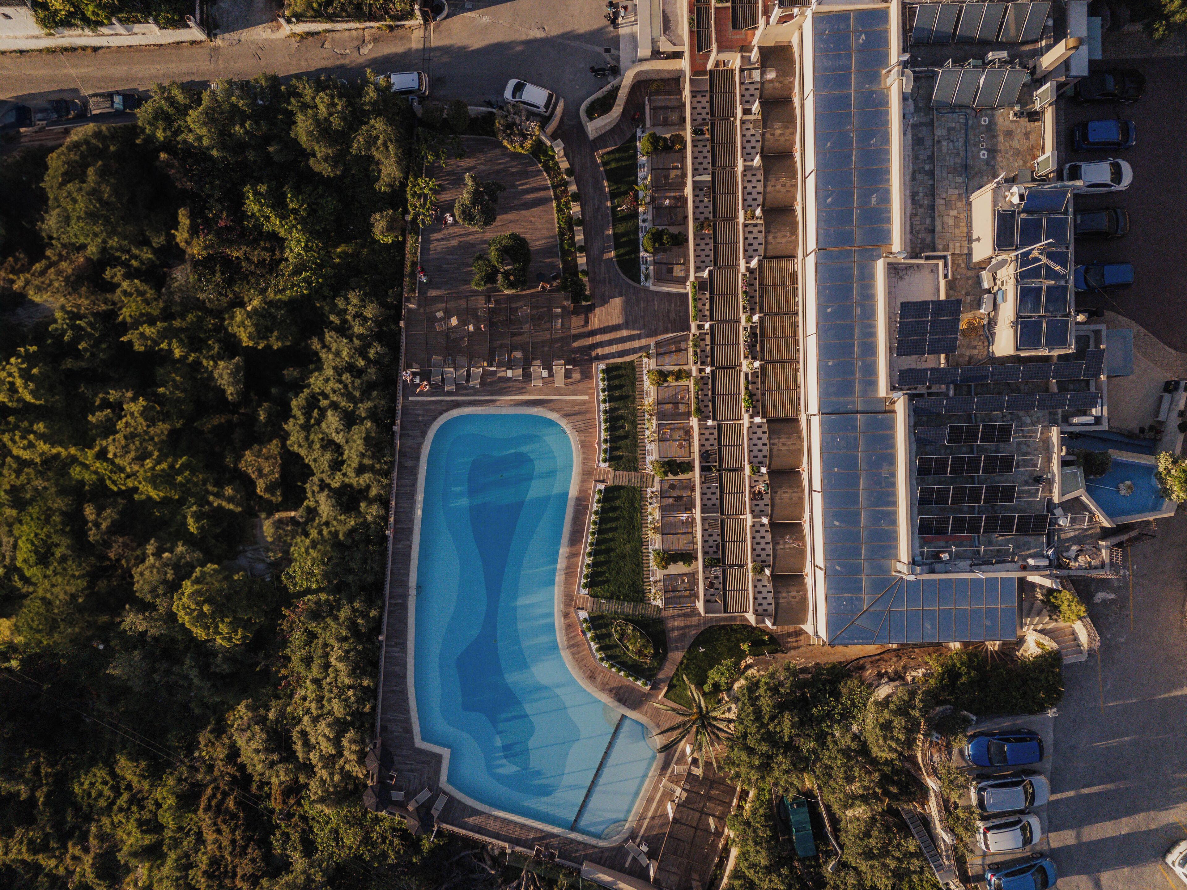 An aerial view of a resort with a swimming pool, solar panels, and a parking area.