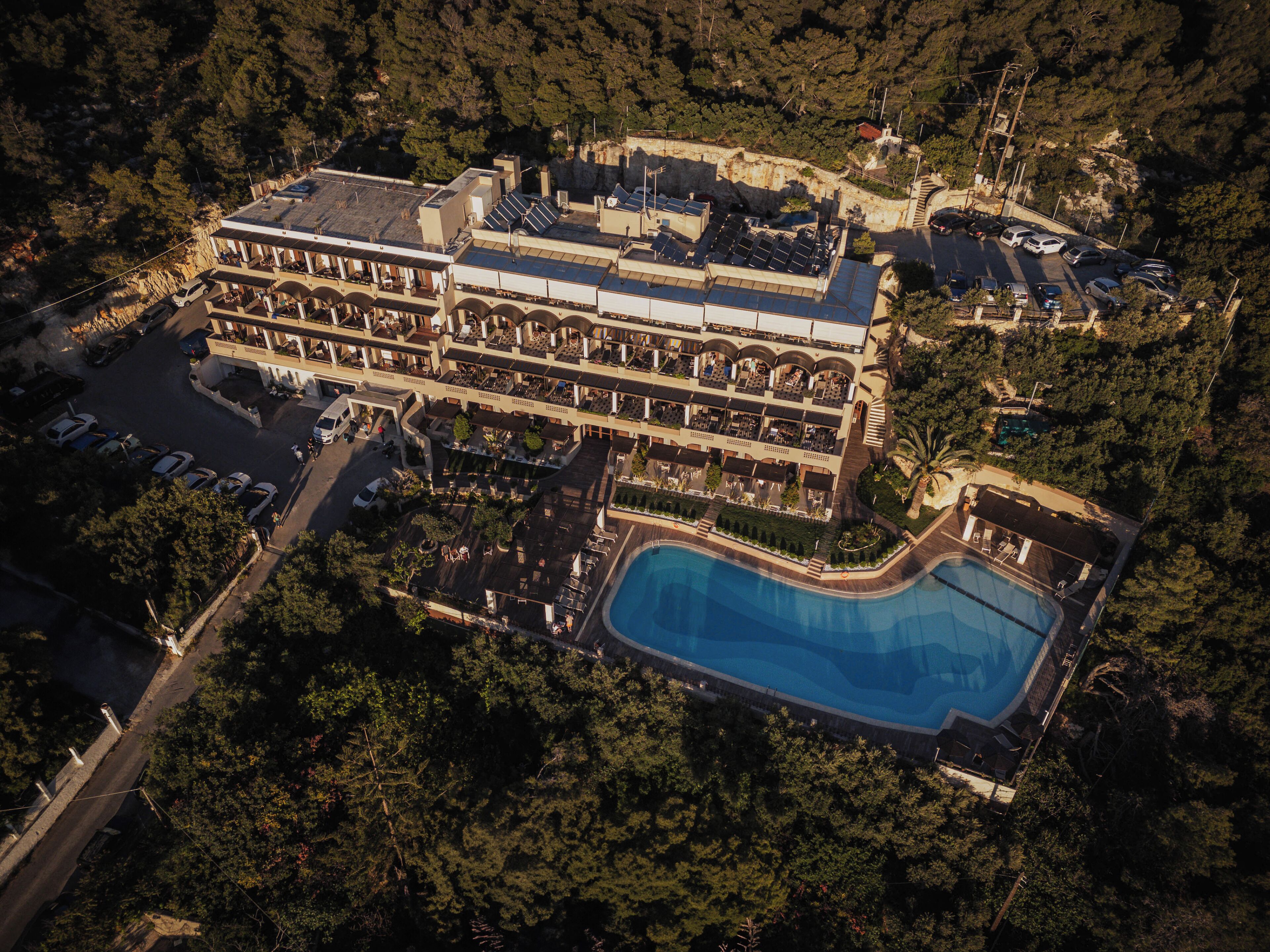 An aerial view of a resort with a large pool, multiple balconies, and a parking area.