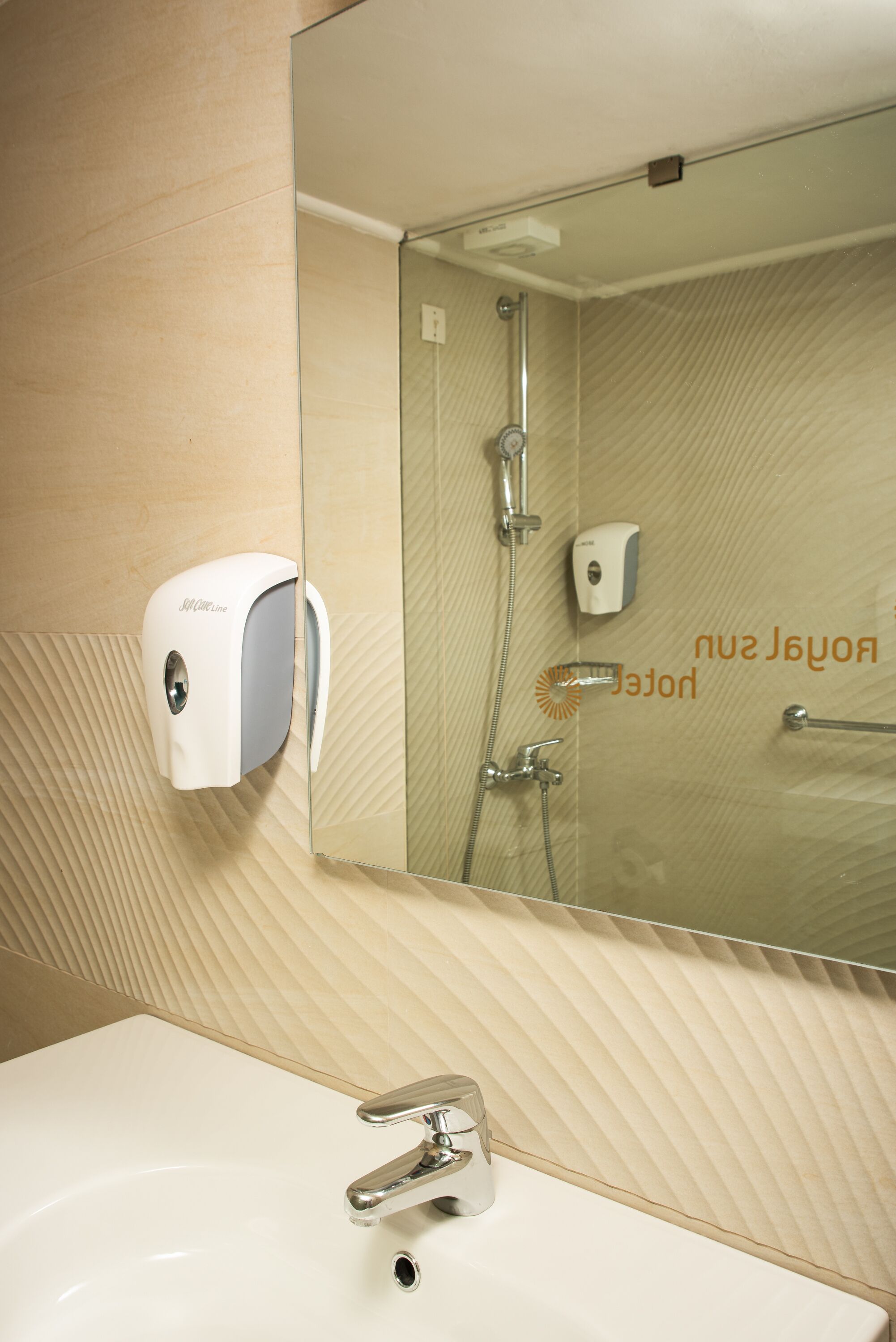 Un baño con lavamanos, dispensador de jabón, ducha y espejo.