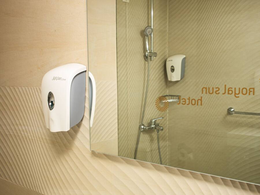 A bathroom with a sink, a hand soap dispenser, a shower, and a mirror.