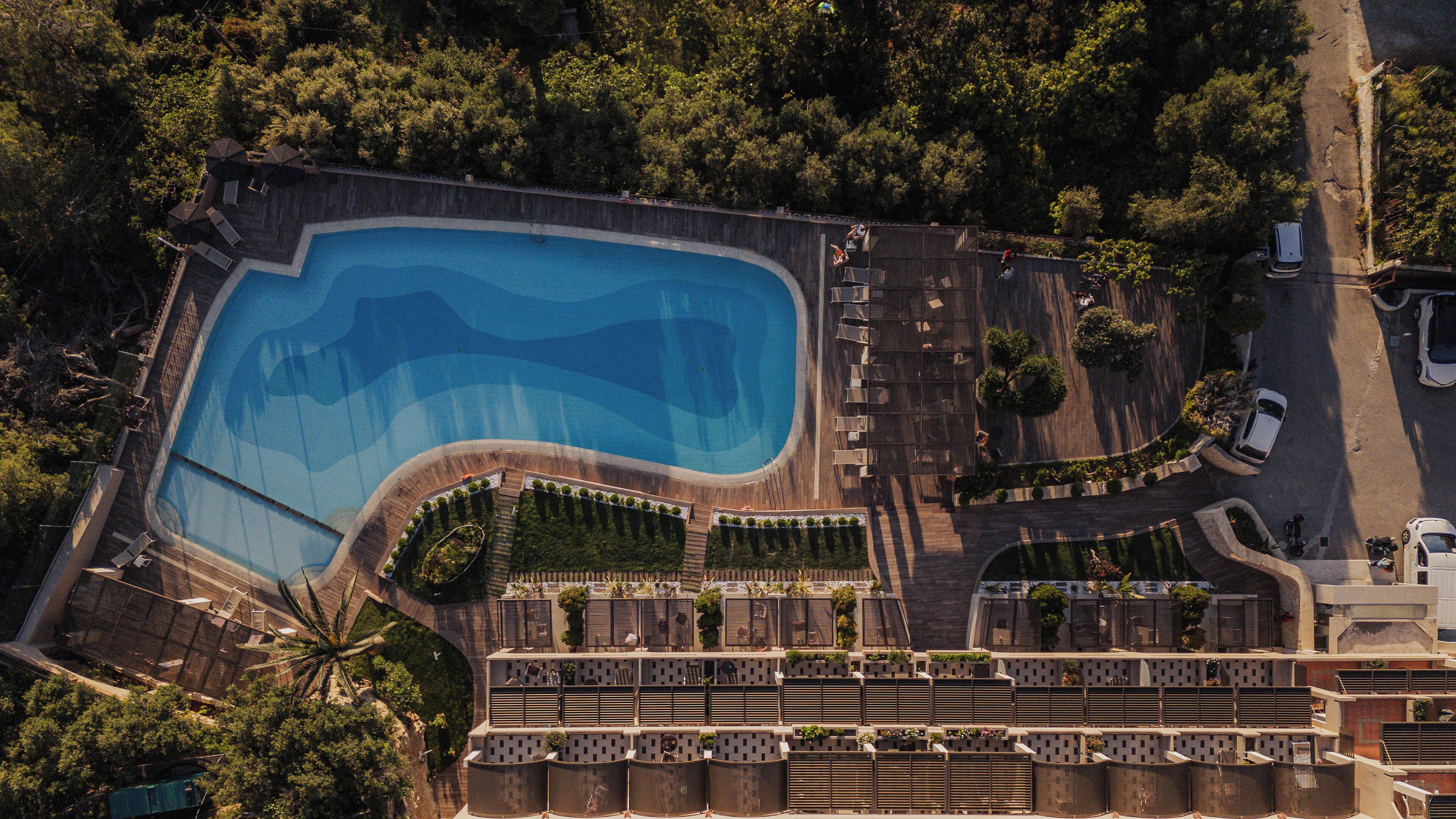 Vue aérienne d’un complexe hôtelier doté d’une grande piscine, de plusieurs niveaux de balcons et d’un environnement verdoyant.