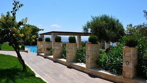 A pathway leading to a pool area with stone pillars and greenery. - Royal Sun Hotel (Chania)