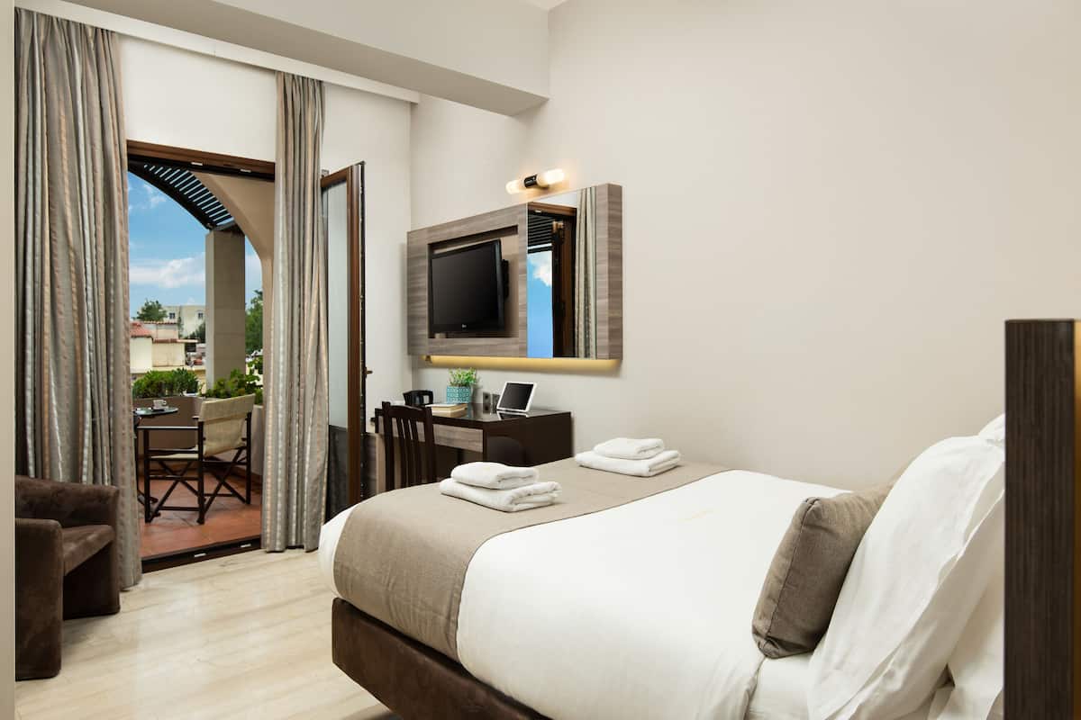 A hotel room with a bed, a desk with a laptop, a TV mounted on the wall, and a view of the outside.