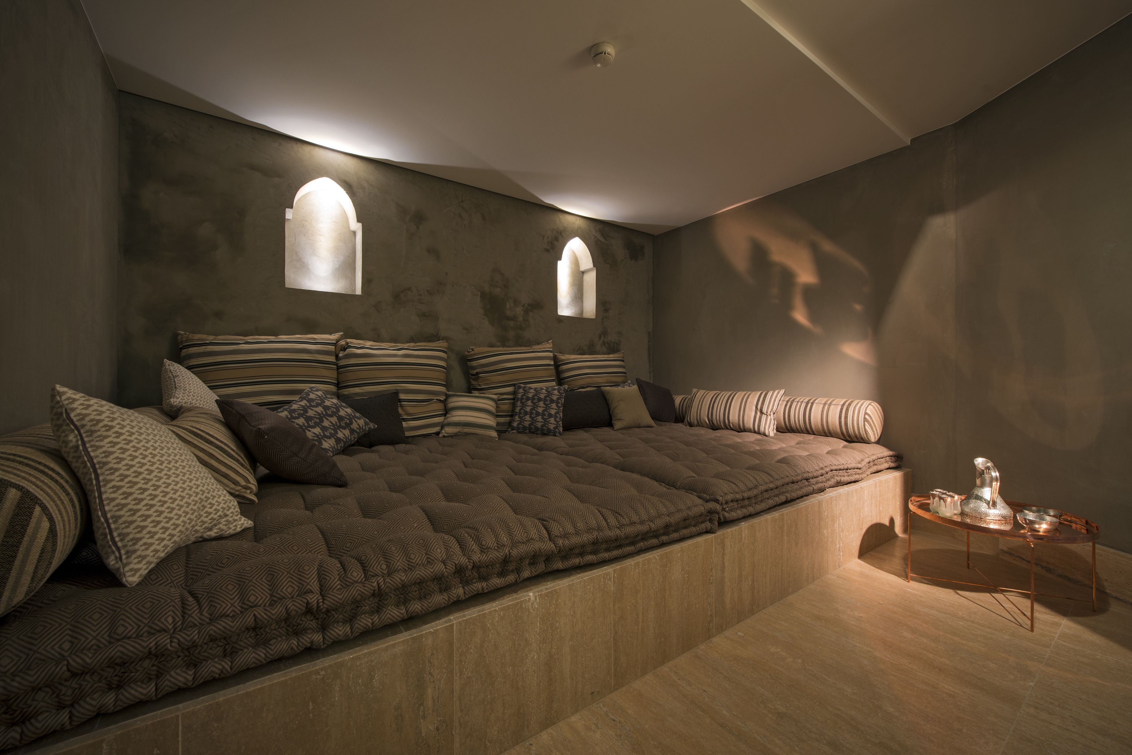 A cozy bedroom with a large bed, two arched windows, and a small table with a lamp.