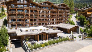 A multi-story wooden hotel with balconies, outdoor seating, and a view of mountains. - La Cordée des Alpes (Bagnes)