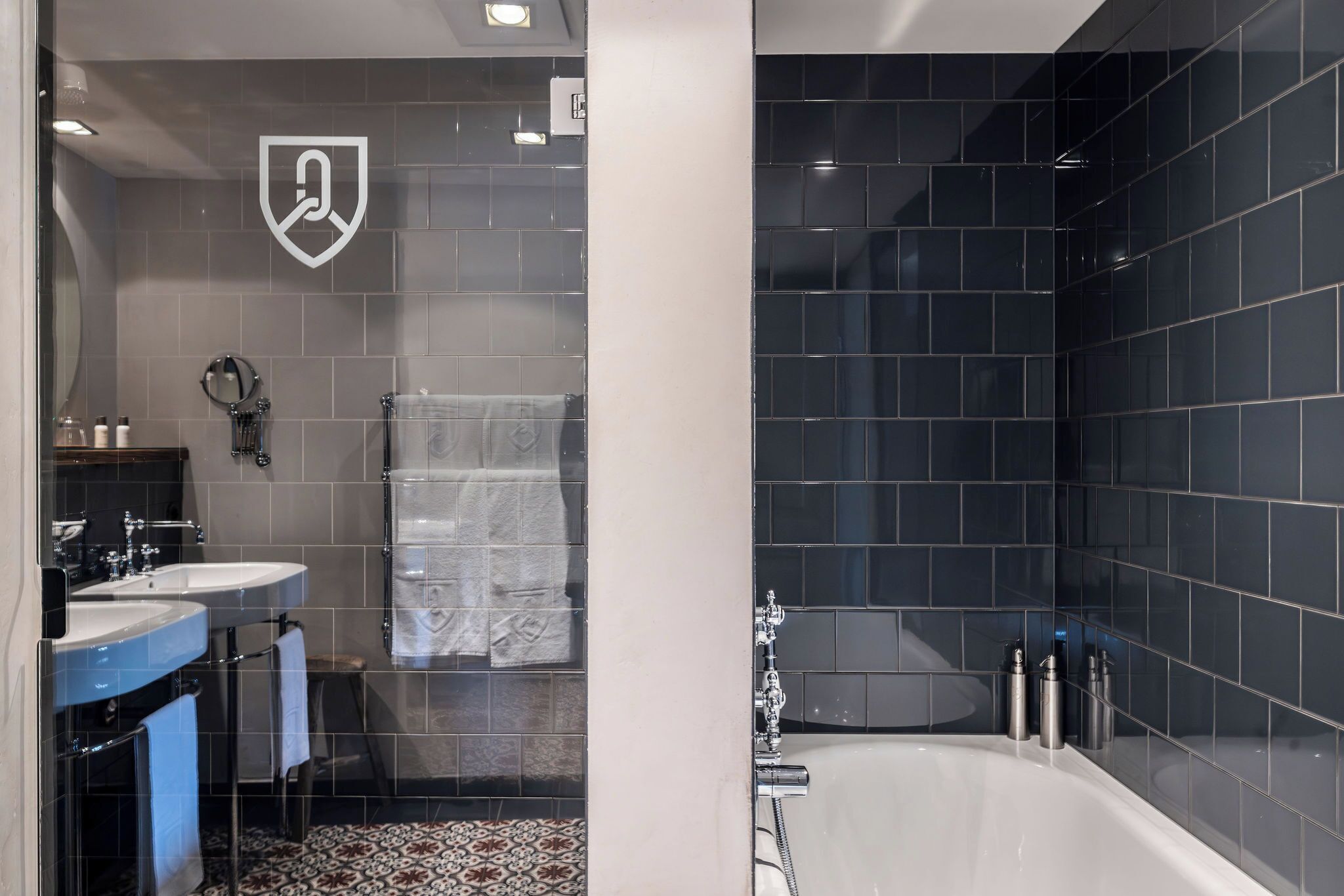 A modern bathroom with dark tiles, a bathtub, and a vanity with two sinks.