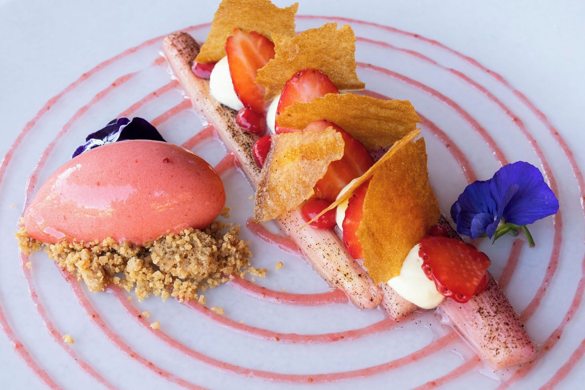 A dessert with strawberries, whipped cream, and crumbled biscuit on a white plate with pink stripes.