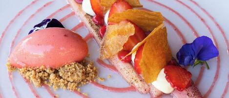 A dessert with strawberries, whipped cream, and crumbled biscuit on a white plate with pink stripes.