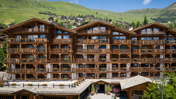A multi-story wooden building with balconies and a mountain backdrop. - La Cordée des Alpes (Bagnes)