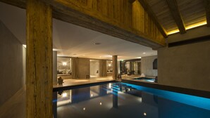 A modern indoor pool with wooden beams, a clear pool surface, and ambient lighting. - La Cordée des Alpes (Bagnes)