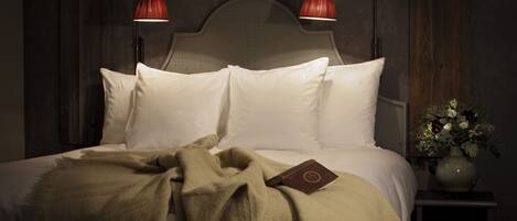A neatly made bed with white linens and a beige throw blanket, two bedside lamps, and a vase with flowers on a nightstand.