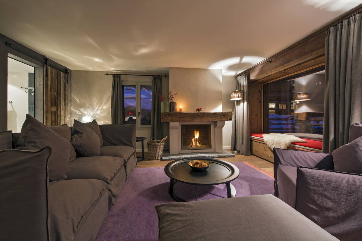 A modern living room with a fireplace, comfortable seating, and a view of the city at dusk.