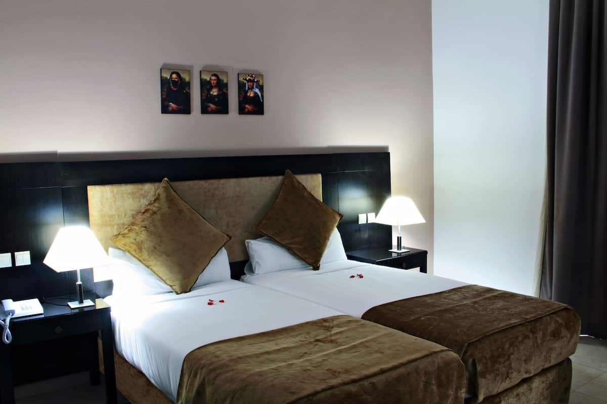Quarto de hotel com uma cama grande, duas mesas de cabeceira, um telefone e três quadros pendurados na parede.