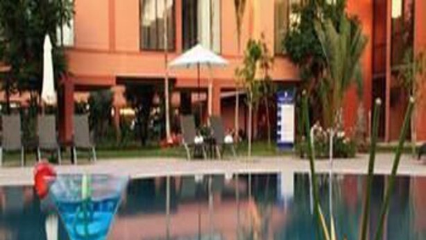 Zona de bar junto a la piscina con vistas despejadas, sillas de descanso y un edificio al fondo.