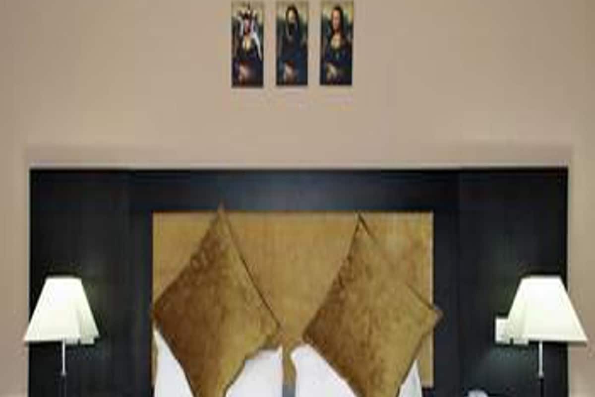 Quarto de hotel com uma cama grande, duas mesas de cabeceira e três quadros na parede.