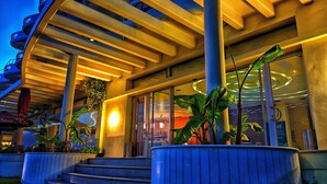 A modern building with a curved facade, large windows, and a well-lit entrance area with steps leading up to the door. - Aegean Blue Beach Hotel (Nea Propontida)