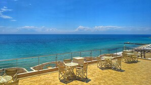 A terrace with outdoor seating overlooking a clear blue sea. - Aegean Blue Beach Hotel (Nea Propontida)