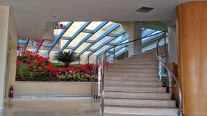 A spacious lobby with a central staircase, a glass ceiling, and a flower garden. - Aegean Blue Beach Hotel (Nea Propontida)