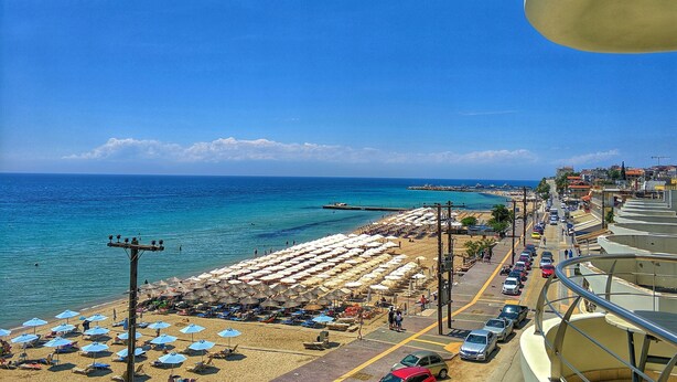 A beach with rows of umbrellas and sun loungers, a clear blue sky, and a view of the sea. - Aegean Blue Beach Hotel (Nea Propontida)