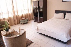 A bedroom with a bed, a chair, a small table with a plant, and a wardrobe.
