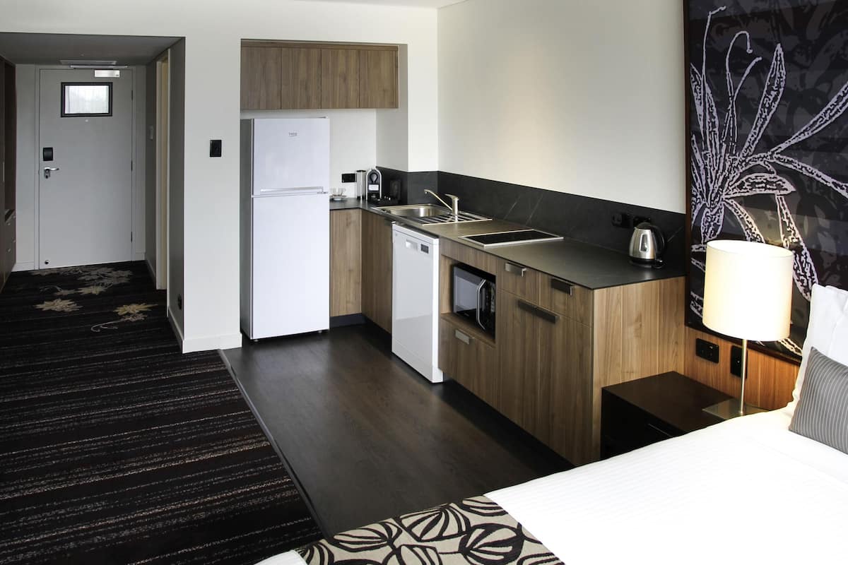 Une chambre d’hôtel moderne équipée d’une kitchenette, d’un lit, d’une table de chevet et d’une grande œuvre d’art abstraite accrochée au mur.