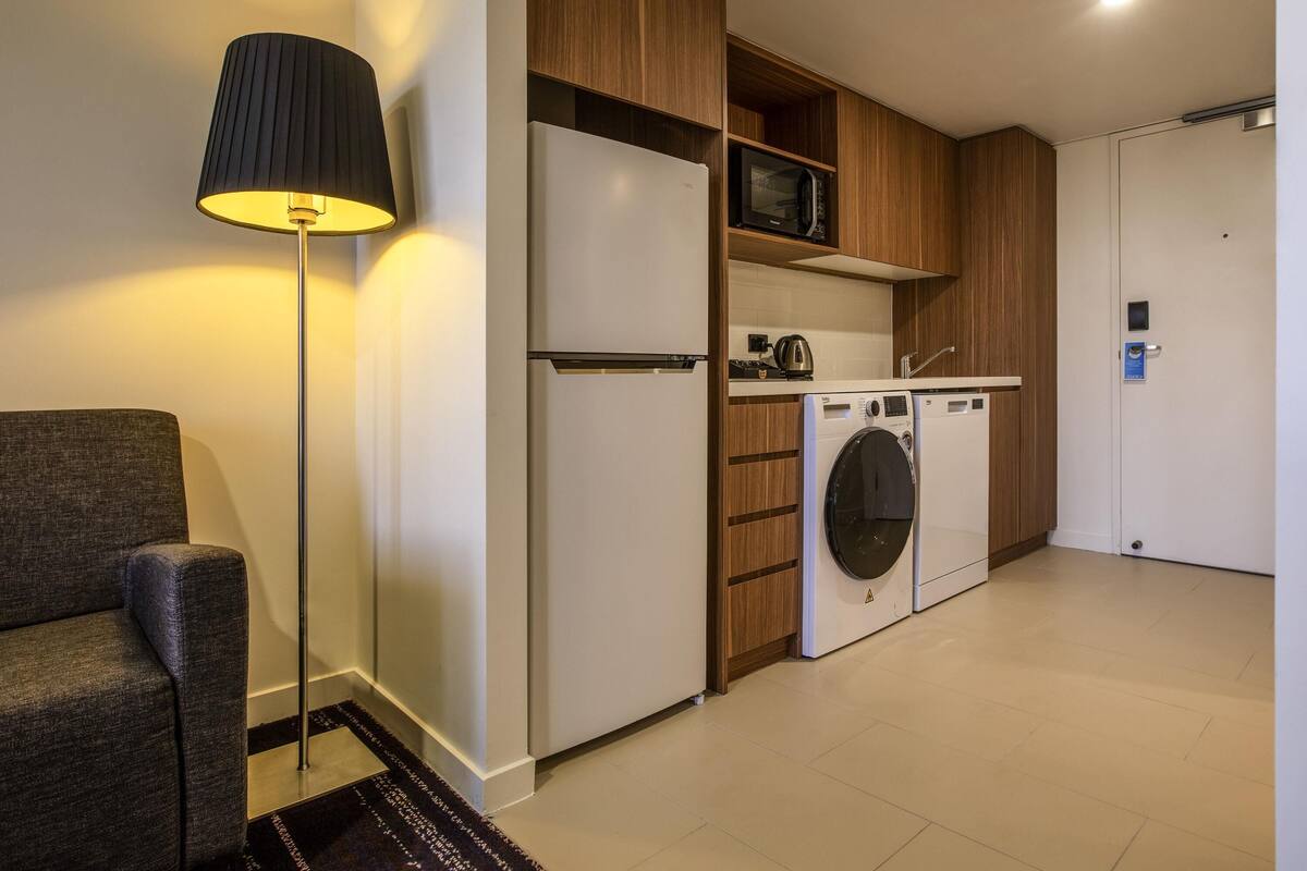 Une petite cuisine équipée comprenant un réfrigérateur, un four à micro-ondes et un lave-linge.