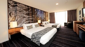 A hotel room with two beds, a desk, a chair, a TV, and a large abstract painting on the wall. - Mantra Gladstone (Barney Point)