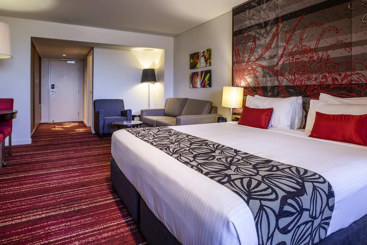 Une chambre d’hôtel avec un grand lit, deux fauteuils, un canapé, un bureau et un mur décoré d’œuvres d’art.