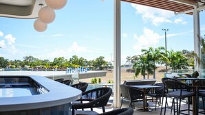 A covered outdoor seating area with tables and chairs, a view of the beach, and a sign with the name 'FONTAINE.' - Mantra Gladstone (Barney Point)