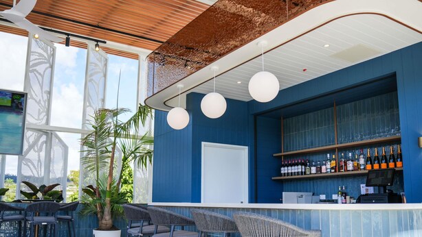 A bar area with a blue wall, a white counter, and several bar stools. - Mantra Gladstone (Barney Point)