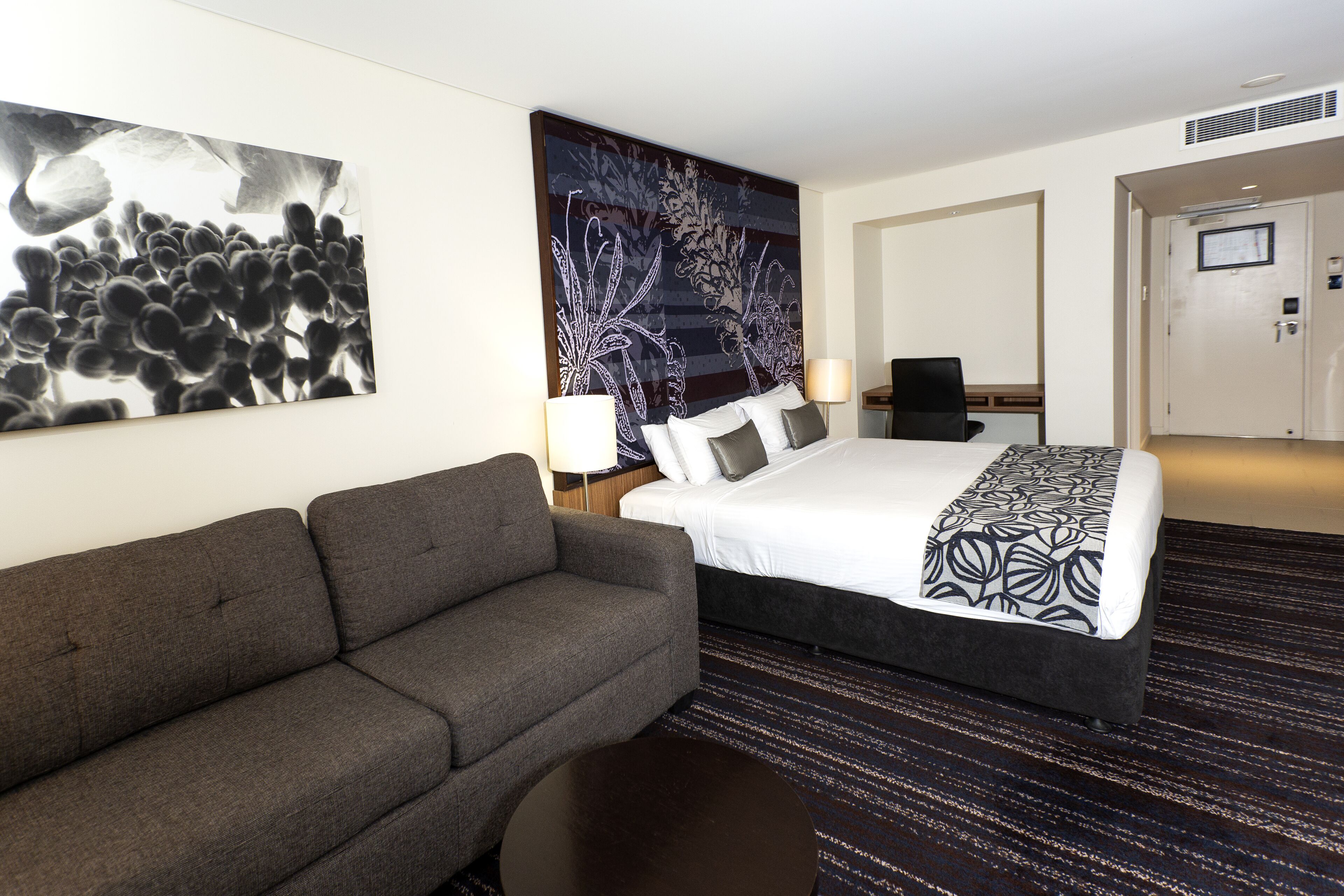 Une chambre d’hôtel avec un grand lit, un canapé gris, une œuvre d’art murale et un sol recouvert de moquette.