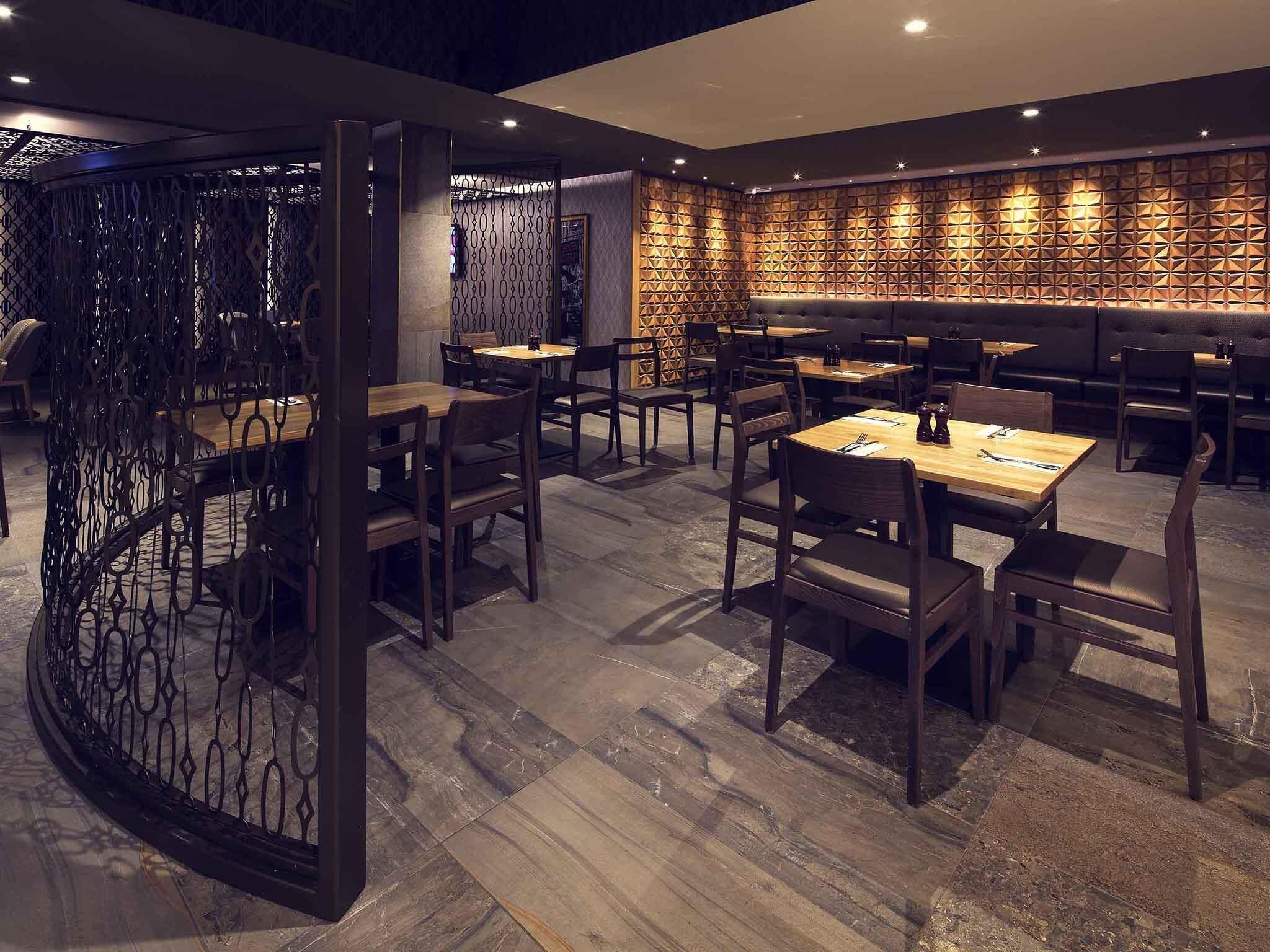Un restaurante con mesas y sillas de madera, un revestimiento mural estampado y una separador metálico decorativo.