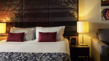 A hotel room with a large bed, two bedside lamps, a chair, a nightstand with a phone, and a wall with a large abstract painting.