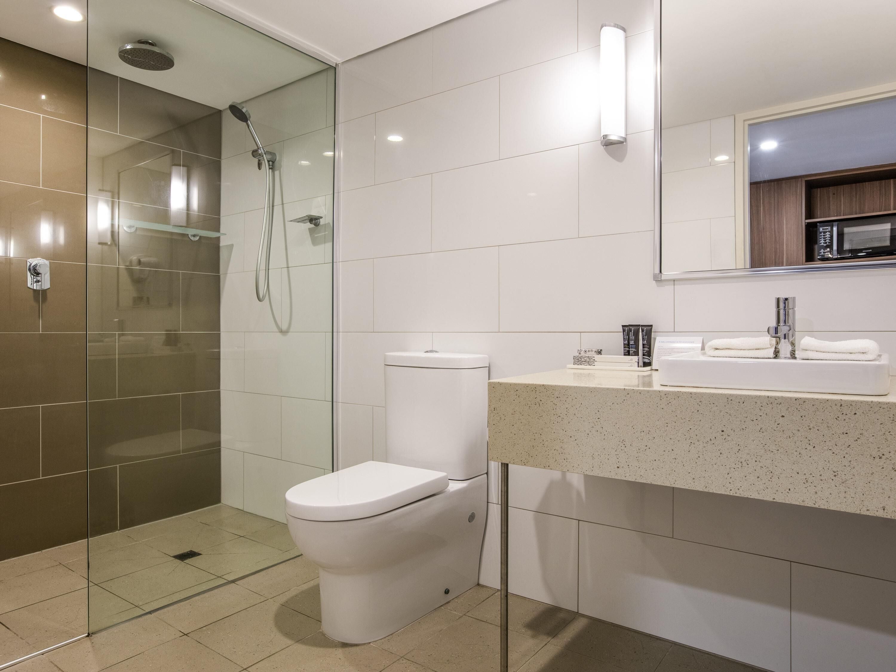 A modern bathroom with a glass-enclosed shower, a white toilet, and a countertop with a sink and mirror.