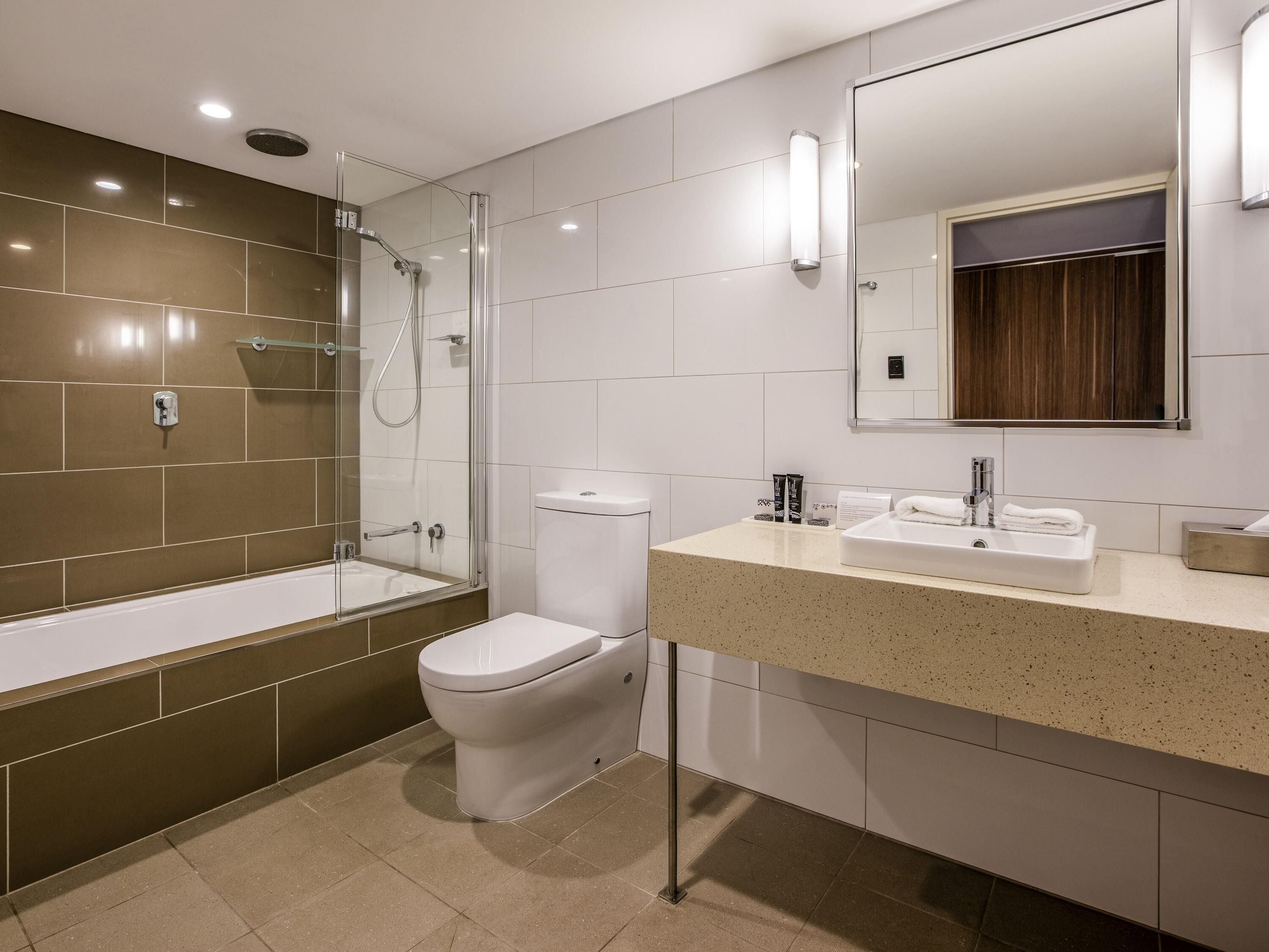 A modern bathroom with a glass-enclosed shower, a toilet, and a sink with a mirror above.