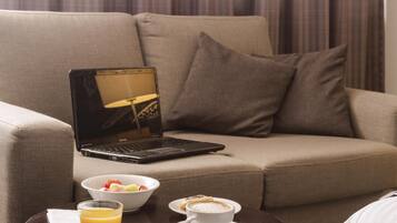 Un ordinateur portable sur un canapé, un verre de jus d’orange, un saladier de fruits et une tasse de café sur une petite table.