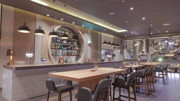 Eine moderne Bar mit einer Holztresore, mehreren hängenden Pendelleuchten und verschiedenen Sitzmöglichkeiten, darunter Barhocker und Tische.