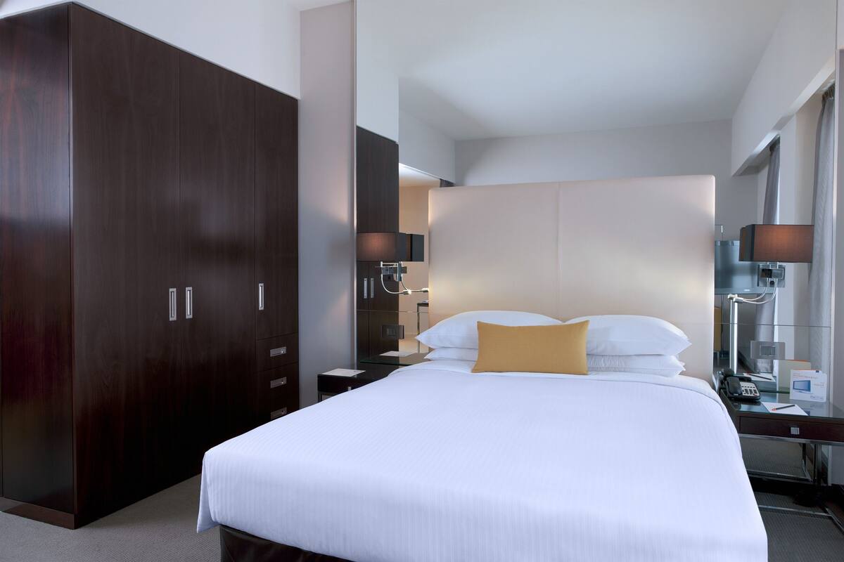 Una habitación de hotel con una cama grande, un armario, una mesita de noche, una lámpara y un espejo.