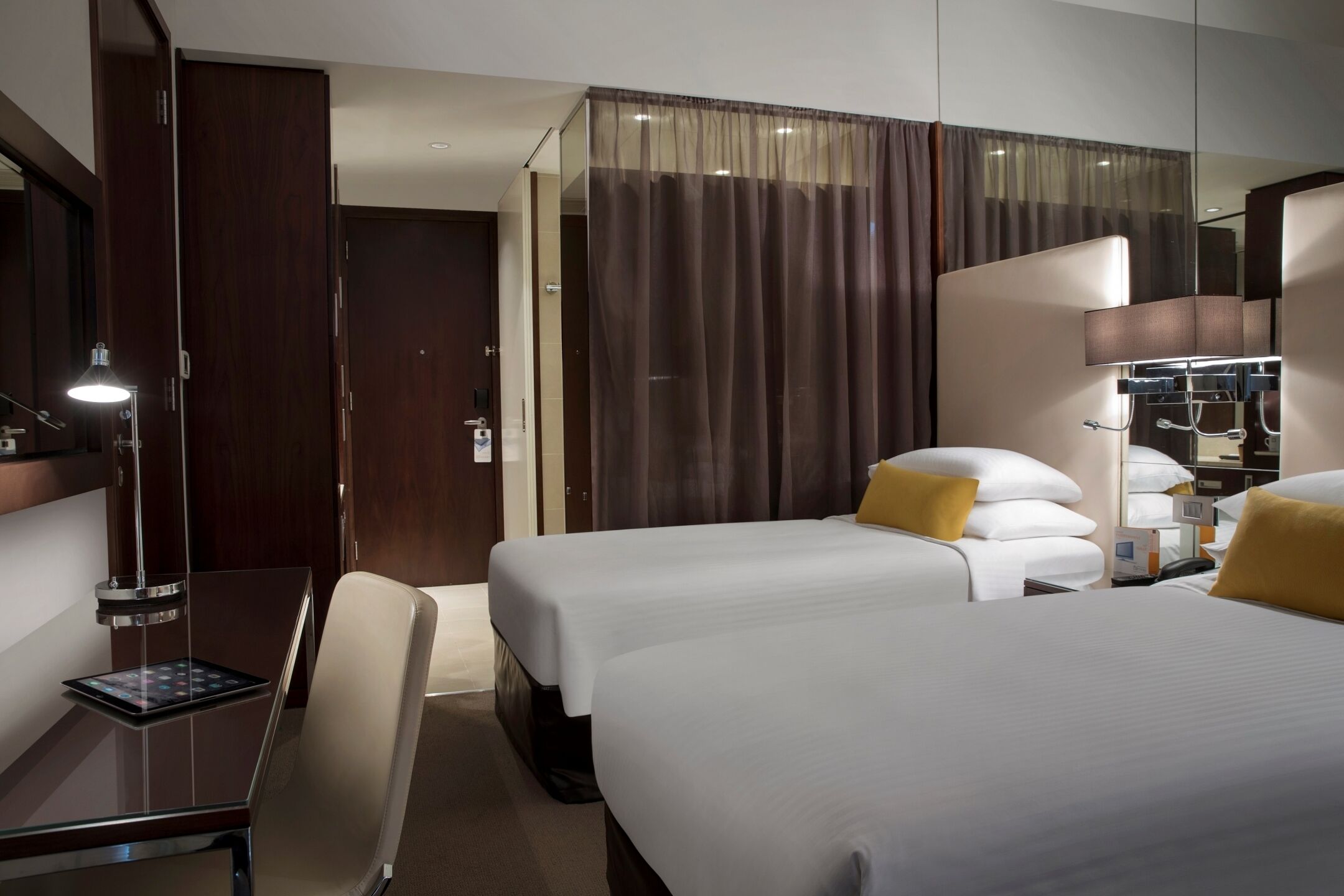 Habitació d'hotel amb dos llits, una taula de treball amb una làmpada i un mirall.