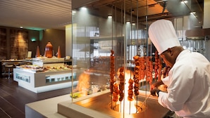 A chef grilling skewered meat in a modern kitchen with a buffet area visible in the background. - Centro Capital Centre (Abu Dhabi)