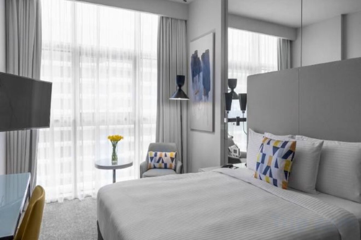 A modern hotel room with a large bed, a desk, and a chair. There is a small table with a vase of flowers.