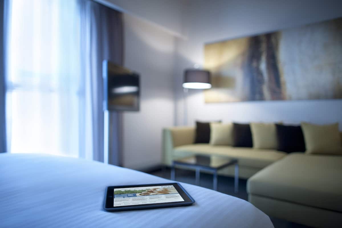 Habitación de hotel con cama, una tablet sobre la cama, sofá y un cuadro en la pared.