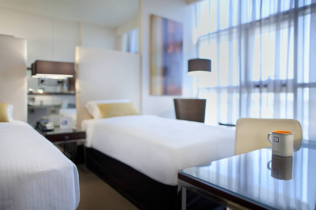 Habitación de hotel con dos camas, un escritorio, una silla, una cafetera y una lámpara.