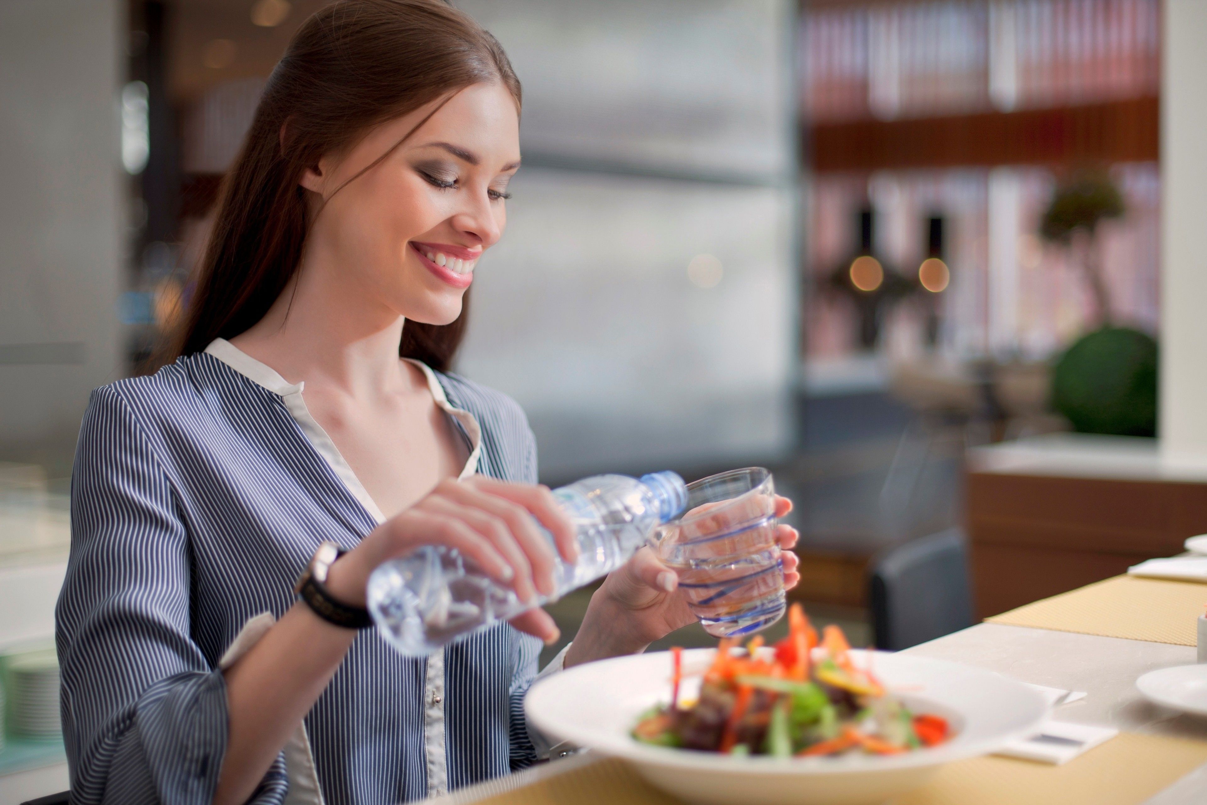 A person pouring water into a glass at a dining table with a plate of food.