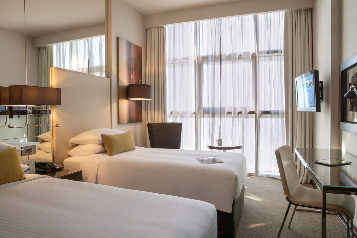 Habitación de hotel con dos camas, un escritorio, una silla, un televisor y una ventana con cortinas.
