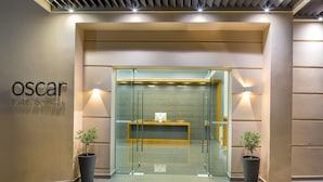 A reception area with a glass partition, a reception desk, and two potted plants. - Oscar Suites & Village (Chania)